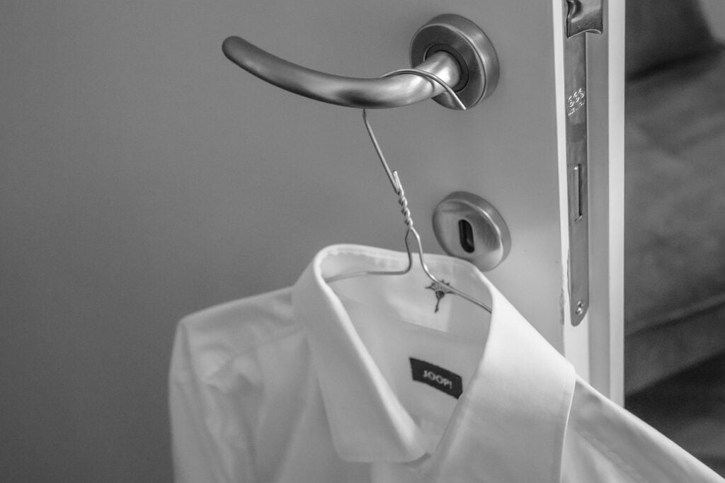Mit einem Dampfglätter geglättetes weißes Hemd auf einem Drahtbügel an einer Türklinke