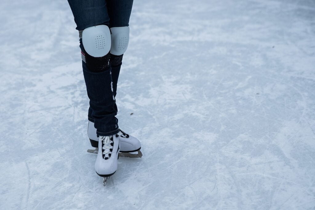 Beine in Schlittschuhen und mit Knieschonern auf dem Eis